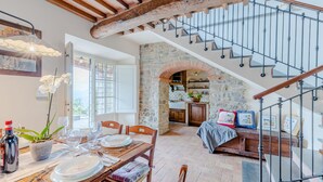 A dining area with a table set for four, a kitchen with stone walls, and a staircase with a wooden railing. - Tuscan Fizz, a traditional Stone Farmhouse with Private Pool and Amazing View among the Vineyards in Lucca (Lucca)