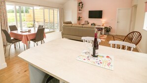 A cozy living room with a sofa, a TV mounted on the wall, and a dining area with a table and chairs. - Y Beudy (Caernarfon)