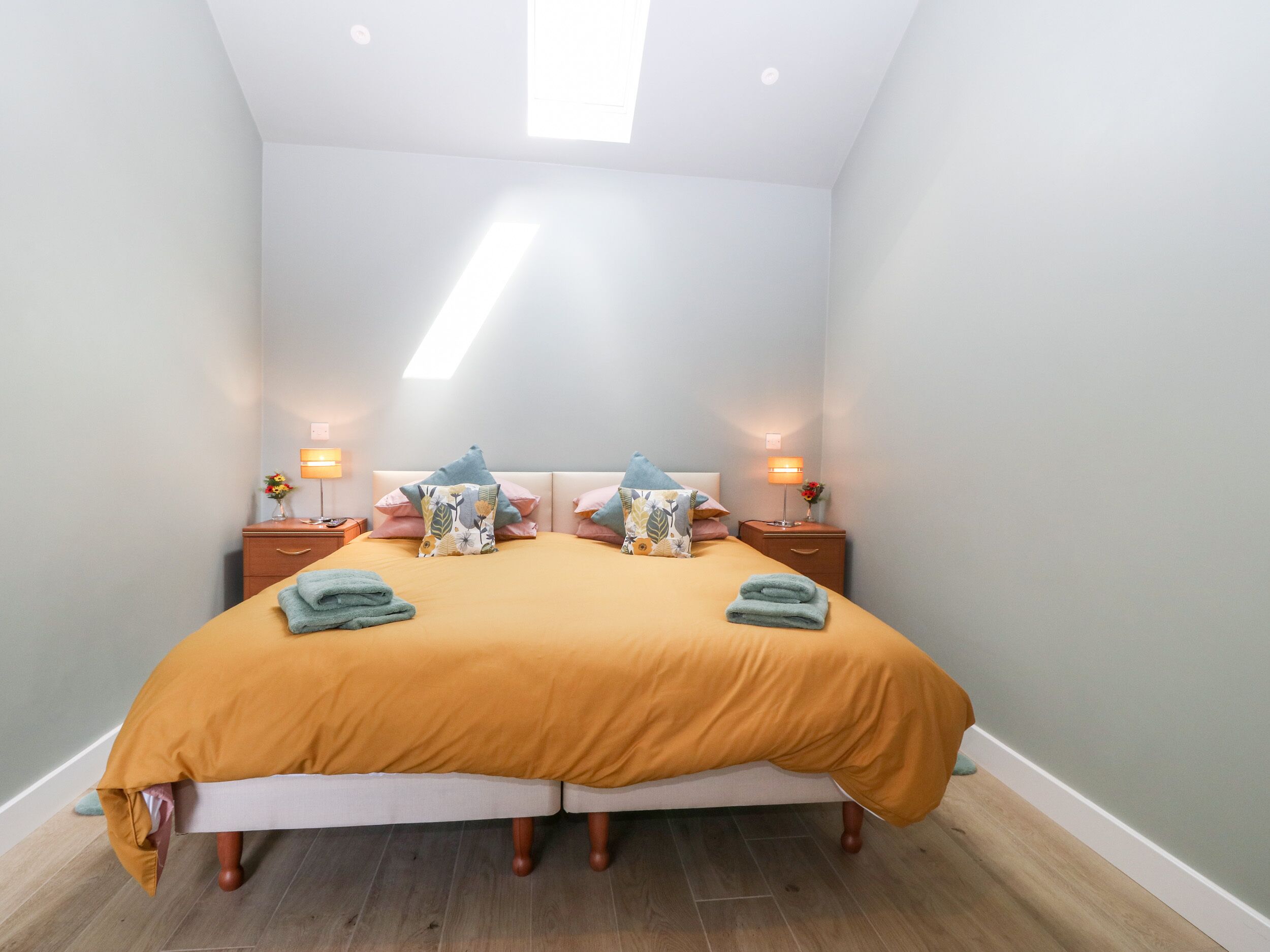 A double bed with a mustard-colored duvet, two bedside tables with lamps, and a skylight above.