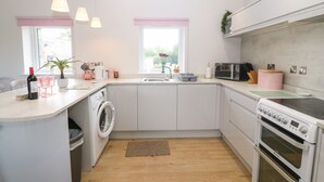 A modern kitchen with a washing machine, a microwave, and a stove. - Y Beudy (Caernarfon)