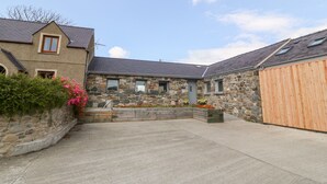 A stone building with a sloped roof and a wooden fence. - Y Beudy (Caernarfon)