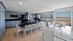 Una cocina moderna con una isla grande, sillas blancas y vistas a la playa.