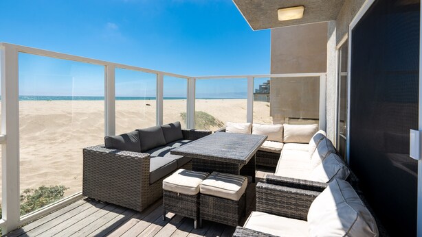 Un balcón con mobiliario de mimbre, una mesa y vistas a la playa.