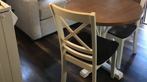 Ein gemütliches Zimmer mit einer holzverkleideten Wand, einem beigen Sofa mit gestreiften Kissen, einem runden Holztisch und weißen Stühlen.
