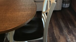 Ein gemütliches Zimmer mit Holzboden, einem beigen Sofa mit gestreiften Kissen, einem runden Holztisch und einem weißen Stuhl.
