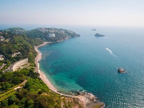 An aerial view of a coastal area with a curved road, a beach, and a mountainous landscape in the background. - Lovely Stunning 2-bed Cottage in Torquay (Torquay)
