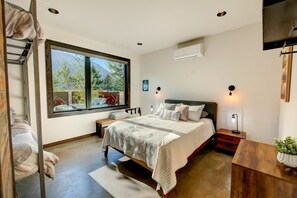 A bedroom with a large window, a bed, bedside tables, and a TV mounted on the wall. - Base Camp 49 - Flagg Mountain Cabin 7B (Mazama)