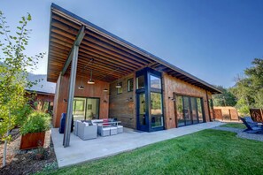 Une maison moderne avec un toit en pente, de grandes portes vitrées et un patio agrémenté de mobilier d’extérieur.