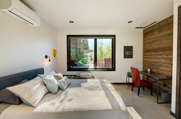 A modern bedroom with a large bed, a desk, and a window.
