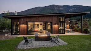 Une maison moderne dotée d’une grande porte vitrée, d’un foyer extérieur et d’un espace salon aménagé à l’extérieur.