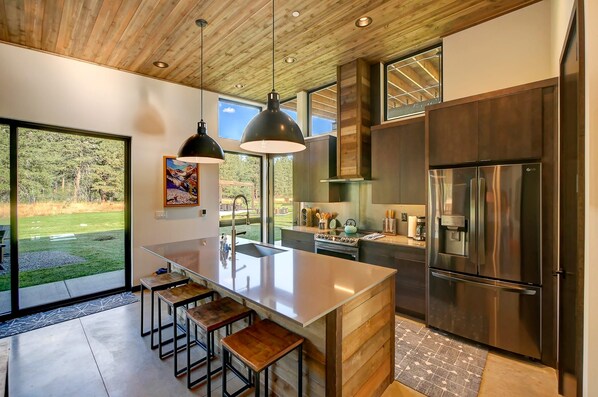 A modern kitchen with a large island, stainless steel appliances, and a view of a grassy area.