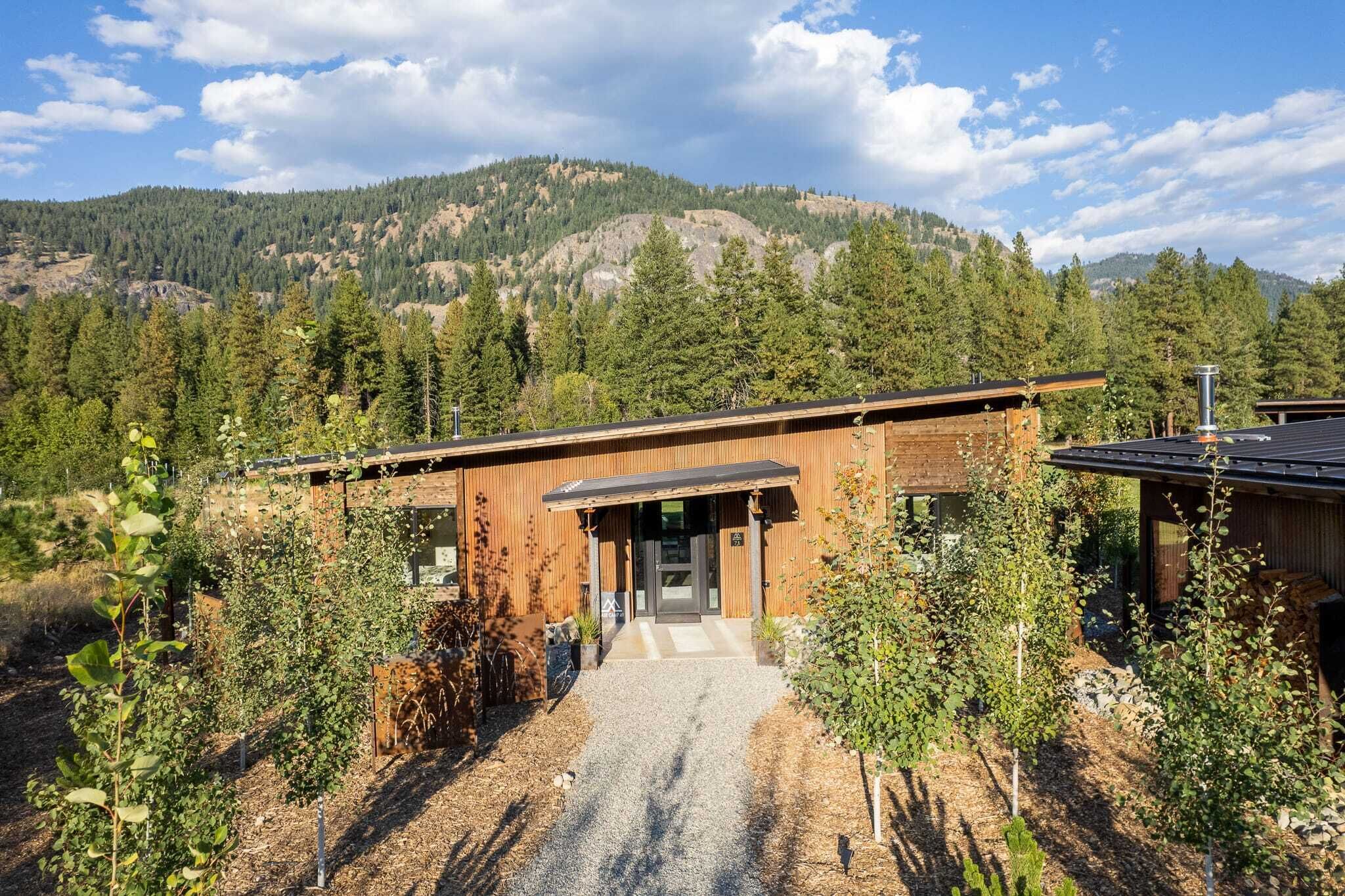 Un bâtiment moderne à l’extérieur en bois, entouré d’arbres et adossé à un paysage montagneux.