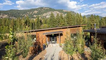Un bâtiment moderne à l’extérieur en bois, entouré d’arbres et adossé à un paysage montagneux.