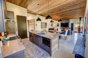 A modern kitchen with a central island, pendant lighting, and a dining area with a view. - Base Camp 49 - Lucky Jim Cabin 11B (Mazama)