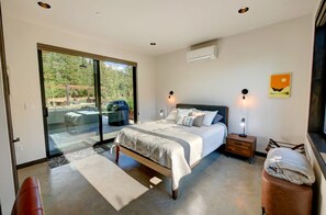 A modern bedroom with a large bed, a glass door leading to a balcony, and a small bedside table with a lamp. - Base Camp 49 - Lucky Jim Cabin 11B (Mazama)