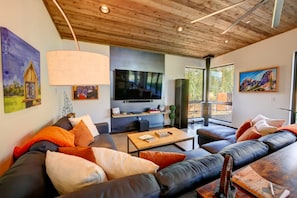 A modern living room with a large flat-screen TV, leather sofas, and a wooden ceiling.
