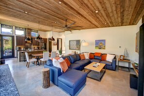 A modern living room with a sectional sofa, a coffee table, and a dining area with a kitchen in the background.