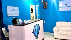 A reception area with a white desk, a white sofa, and two signs on the wall. - Pousada Turquesa by Gente Bonita (Búzios)