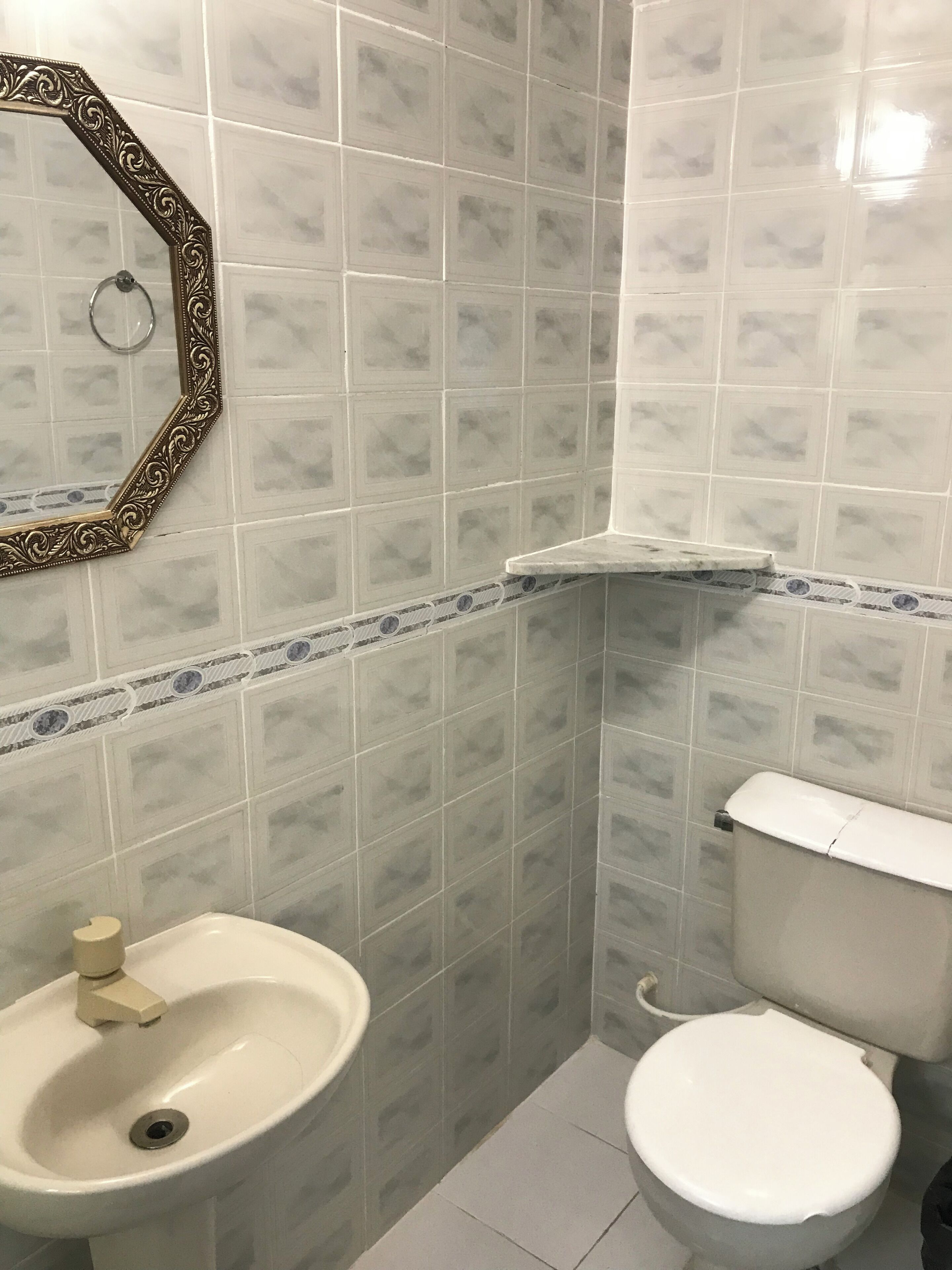 Een badkamer met een wastafel, toilet en een spiegel met een sierlijk frame.