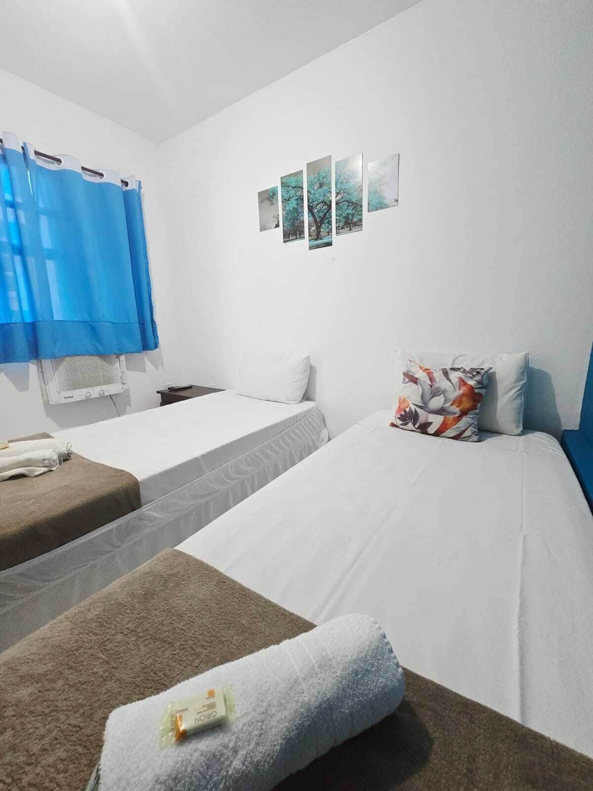 Habitación de hotel con dos camas, una ventana con cortinas azules y una pared con tres cuadros enmarcados.
