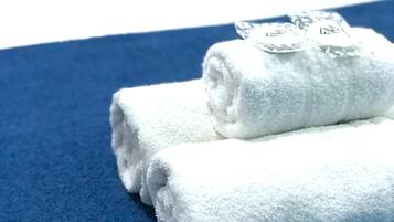 A neatly folded white towel on a blue towel on a bed with a white headboard and a dark blue pillow.
