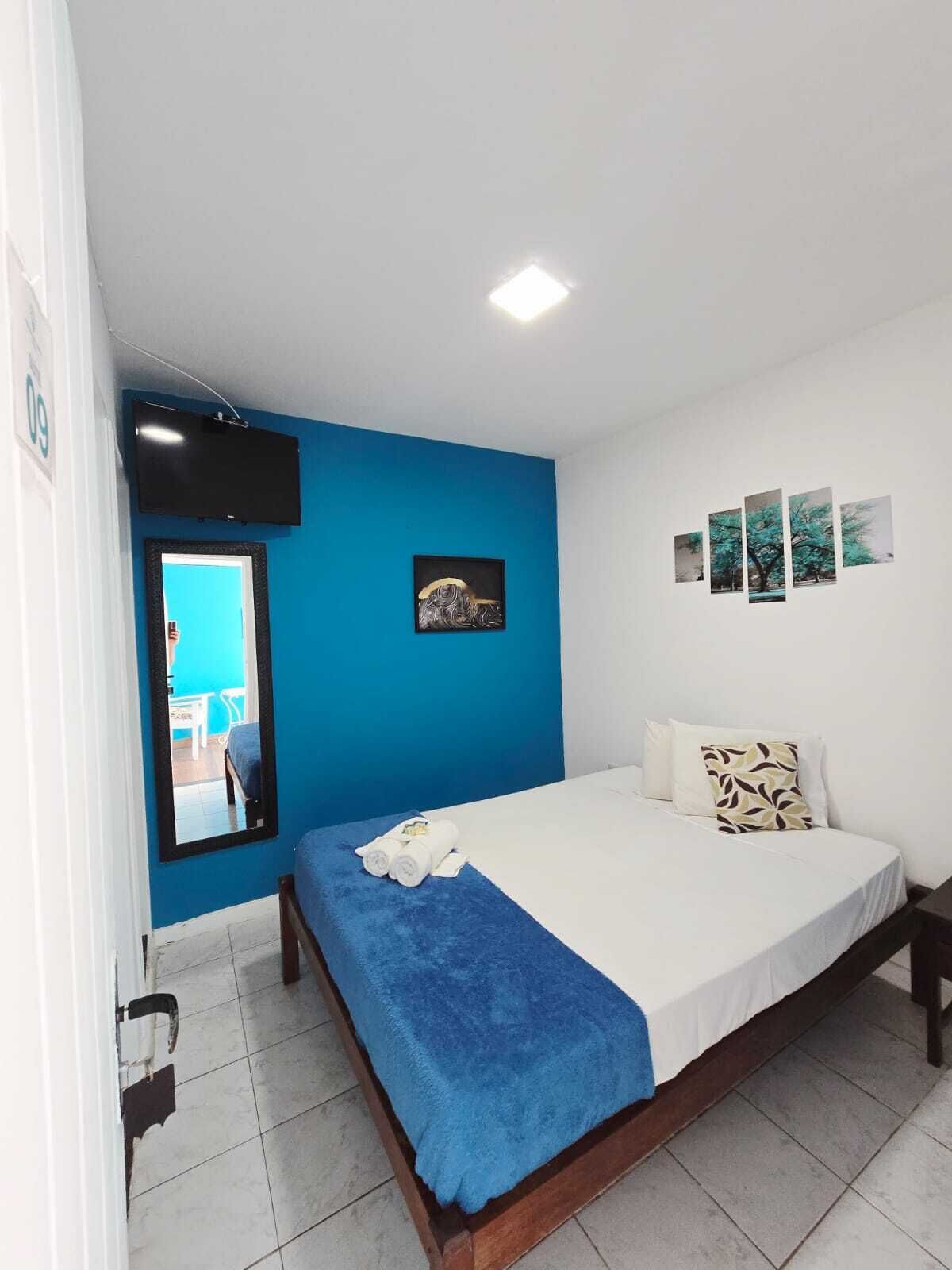 A bedroom with a bed, a mirror, a flat-screen TV, and artwork on the wall.