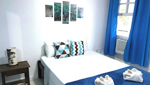 A hotel room with a bed, pillows, a bedside table with a lamp, and a window with curtains. - Pousada Turquesa by Gente Bonita (Búzios)