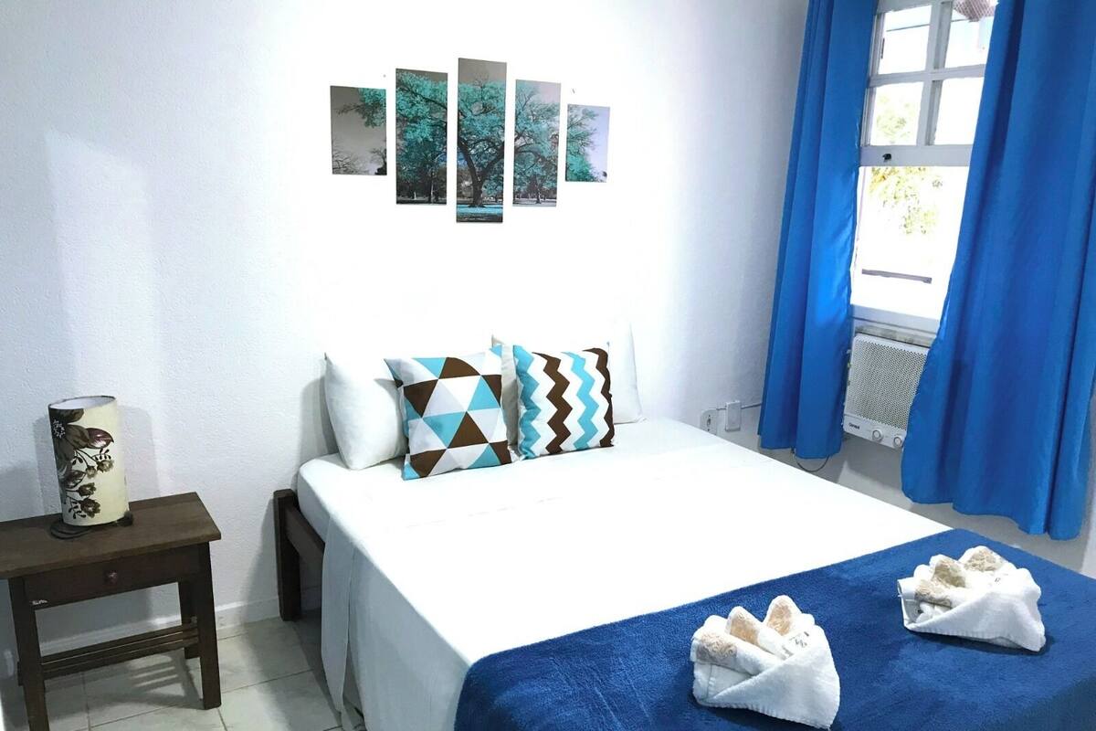 Une chambre d’hôtel avec un lit, des oreillers, une table de chevet avec une lampe et une fenêtre avec des rideaux.