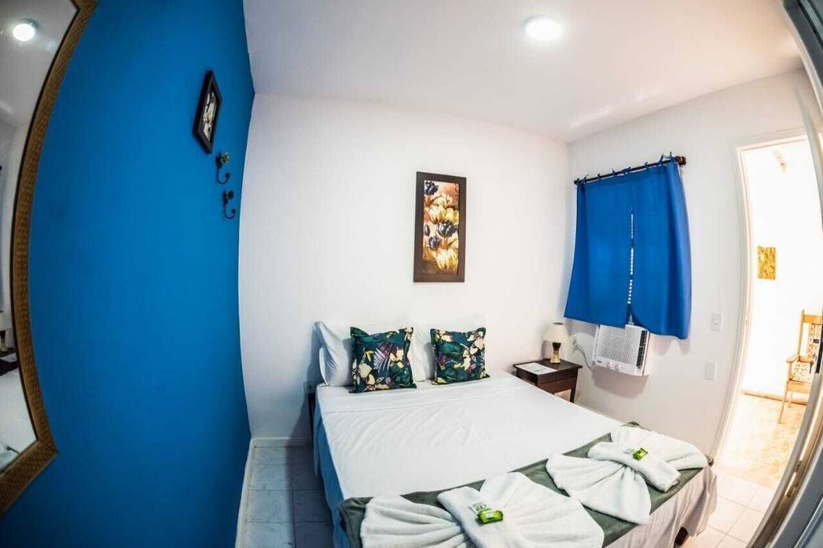 Une chambre d’hôtel avec un lit, une table de chevet, un climatiseur fixé au mur et une fenêtre avec des rideaux bleus.
