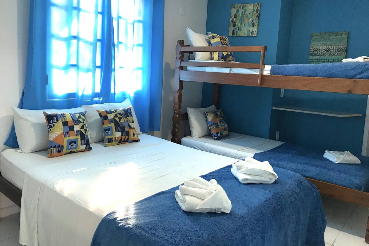 Une chambre avec deux lits, dont l’un est doté d’une tête de lit en bois et l’autre est un lit superposé. Des oreillers sont posés sur les lits, et des serviettes sont également disposées sur les lits.