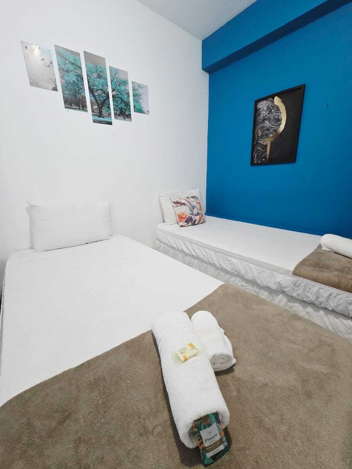 Een hotelkamer met twee bedden, een blauwe accentmuur en drie ingelijste foto's.