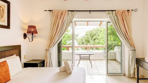Une chambre à coucher avec un lit, une table de chevet, une lampe et une vue sur un balcon extérieur.