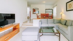 Un salon moderne doté d’un téléviseur à écran plat, d’une table basse en verre, d’un canapé, d’un meuble TV en bois et d’un escalier menant à un niveau supérieur.