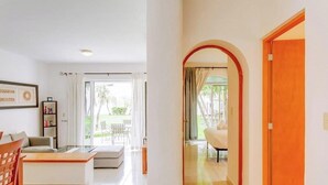 Un salon moderne avec un canapé, une table basse et une bibliothèque. Une porte vitrée donne accès à un espace extérieur comprenant une table et des chaises de patio.
