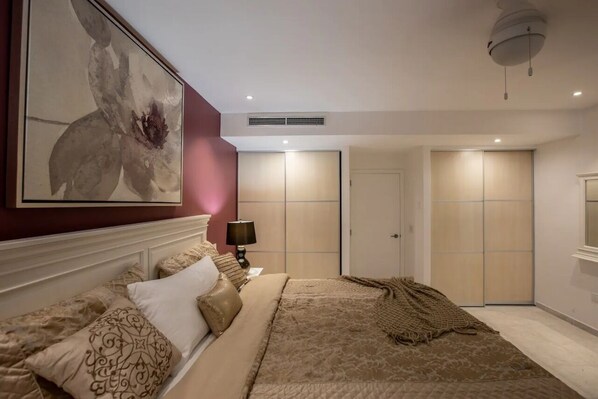 A bedroom with a large bed, a nightstand, a lamp, a ceiling fan, and a wardrobe. - Spacious Garden View Condo (Maho)