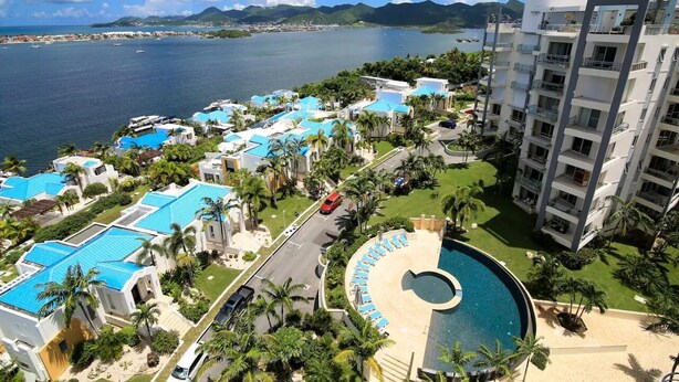 Ein Resort mit mehreren Gebäuden mit blauen Dächern, einem zentral gelegenen Pool und Blick auf den Ozean und die Berge.