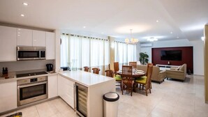 Eine moderne Küche mit Edelstahlgeräten, ein Essbereich mit Holzsesseln, ein Sofa und ein flachbildfernseher an der Wand.