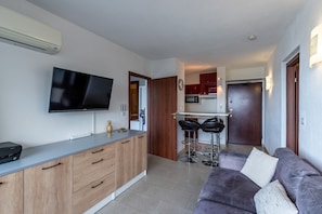 A modern kitchen with a flat-screen TV, wooden cabinets, and a bar area with stools.