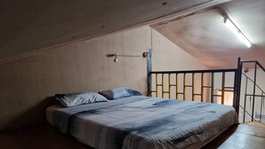 En säng för en person i ett rum med ett sluttande tak och ett litet fönster.
