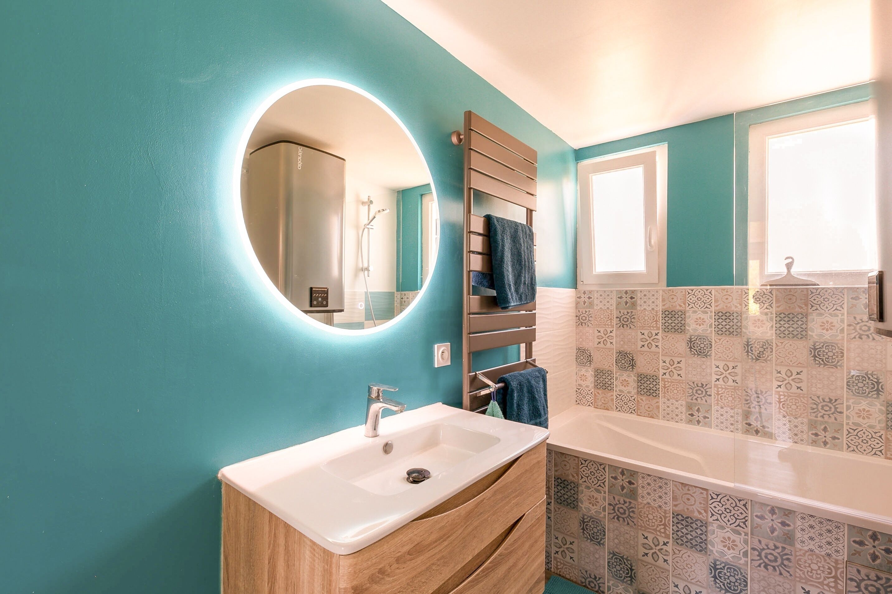 A bathroom with a sink, mirror, towel rack, and patterned tiles.