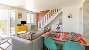 Un comedor con una mesa de madera preparada para cuatro personas, un sofá y una escalera que sube a otro nivel.