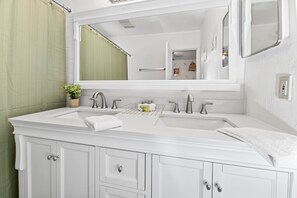 A bathroom with a white vanity, two sinks, a large mirror, and a green shower curtain.