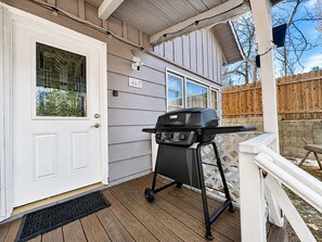Una casa con puerta blanca, una parrilla sobre un soporte y una terraza de madera.