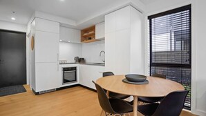 A modern kitchen with white cabinetry, a built-in oven, and a dining area with a round table and chairs.