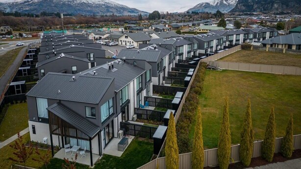 A residential area with modern houses, a grassy field, and mountains in the background.
