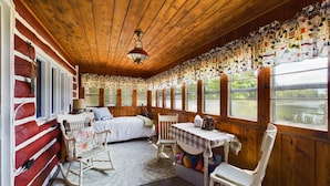 A cozy cabin room with a bed, rocking chair, and table with a checkered tablecloth.