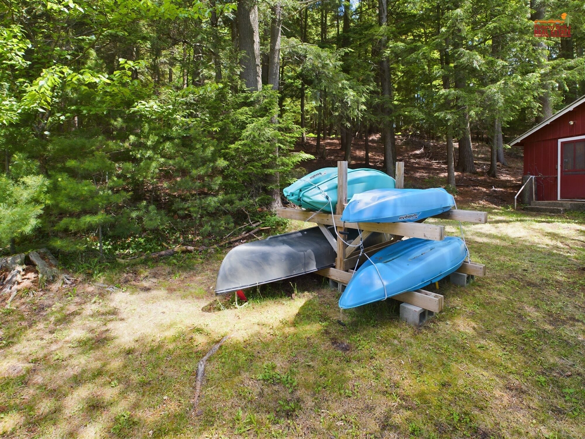 A wooden bench with kayaks and a red shed in a wooded area.