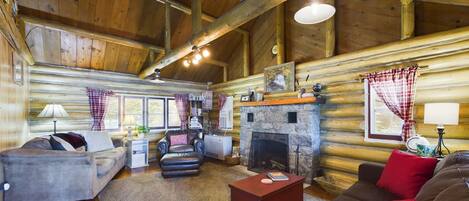 A cozy log cabin interior with a fireplace, wooden walls, and a comfortable seating area.