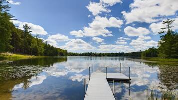 A calm lake with a wooden dock extending into the water, surrounded by dense forest.