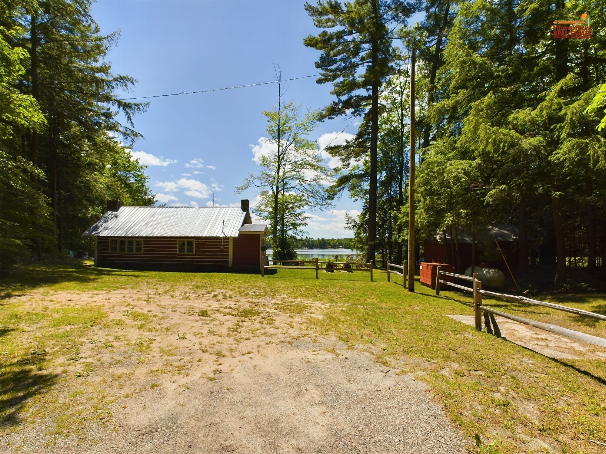 A rustic cabin with a metal roof, surrounded by a grassy area and dense trees.